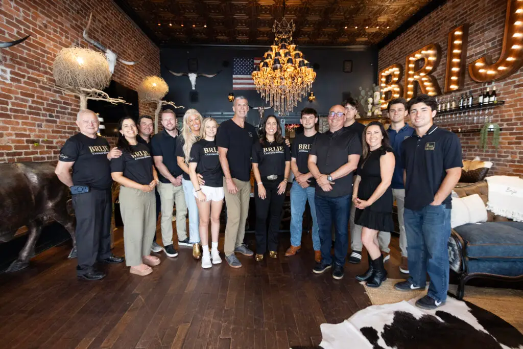 The Brije Custom Homes team inside their downtown Ocala showroom with rustic brick walls and the illuminated BRIJE marquee sign